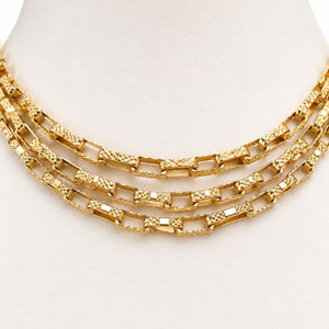 A three-layered gold chain necklace with textured and polished rectangular links, displayed on a white mannequin bust.