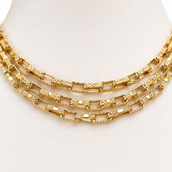 A three-layered gold chain necklace with textured and polished rectangular links, displayed on a white mannequin bust.