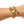 A gold-toned charm bracelet worn on a person's wrist, featuring a lobster clasp, chain links, a padlock charm, and a high-heeled shoe charm, shown against a plain white background.