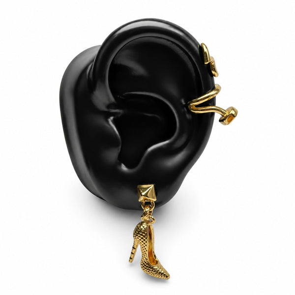 Gold ear cuff and dangling high-heeled shoe charm earrings displayed on a black ear-shaped mannequin against a white background.