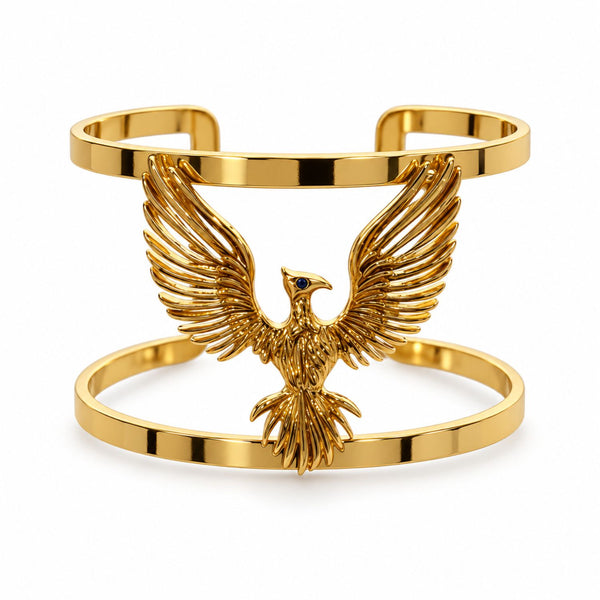 A gold-plated cuff bracelet featuring a detailed eagle with outstretched wings and a small blue eye accent, set against a plain white background.