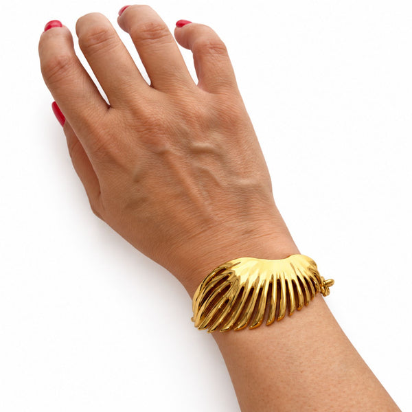 A gold-toned, ribbed wing-shaped cuff bracelet worn on a woman's wrist, shown against a plain white background.