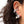 A close-up of a person's ear wearing a cluster of silver-toned ear cuff earrings with clear stones, a black bead, a skull detail, and a dangling white pearl.