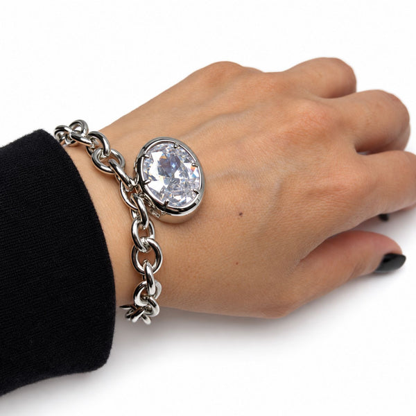 A silver chain bracelet with a large oval clear crystal gemstone, shown worn on a person's wrist against a white background.