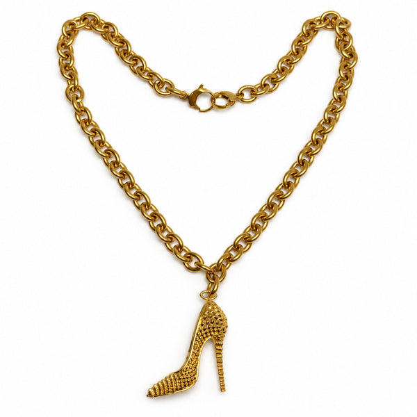 A gold-tone chain necklace featuring a textured, high-heeled shoe charm, displayed against a solid white background.
