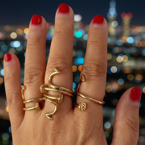 Hand wearing gold nail ring juste clou rings with a cityscape background