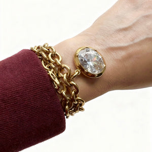 Gold chain bracelet with a large crystal on a wrist against a white background